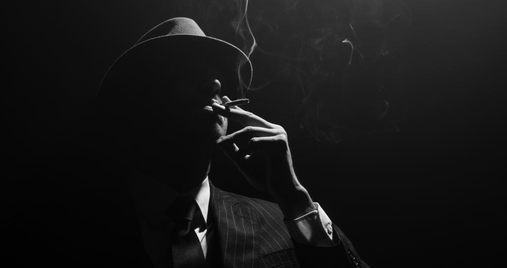 Monochrome image of mafioso silhouette smoking on black backgrou